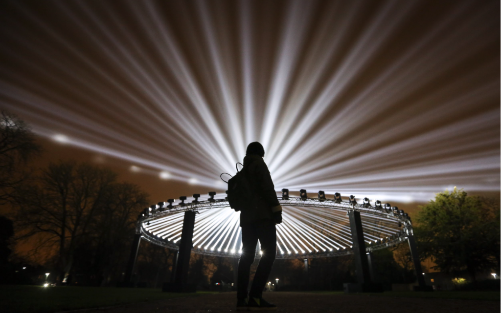 A woman silhouetted by a large ring of lights at night in Lloyd Park, Walthamstow